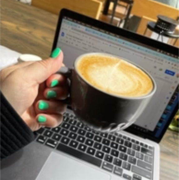 a woman holding a cup of coffee in front of a laptop.