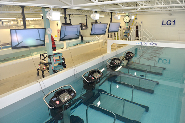 a large swimming pool with underwater treadmills and with lots of monitors on the wall.