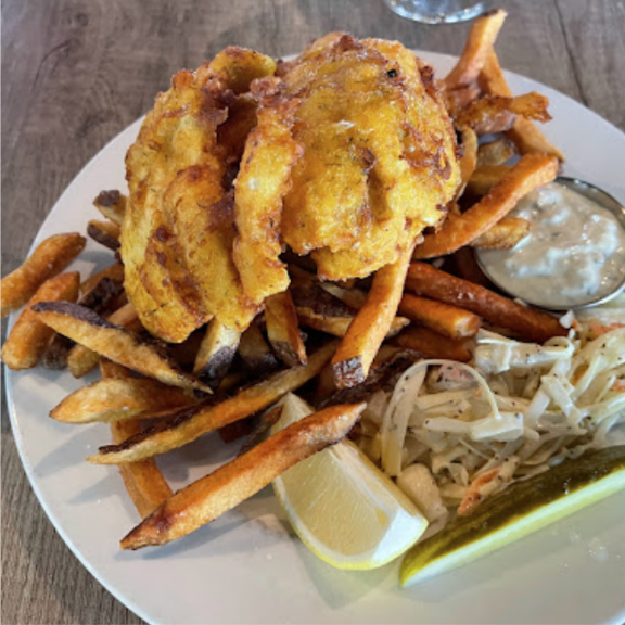 a fish and chips plate topped with fries and coleslaw.