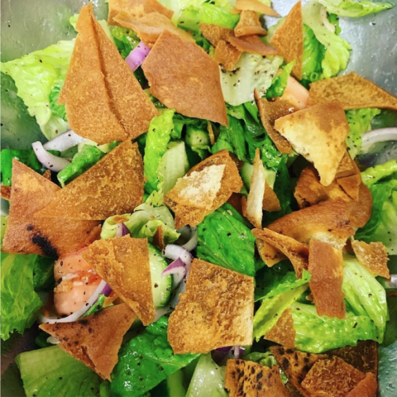 a close up of a salad with lettuce and pita chips.