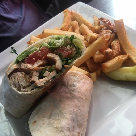 a grilled chicken wrap and french fries on a white plate.