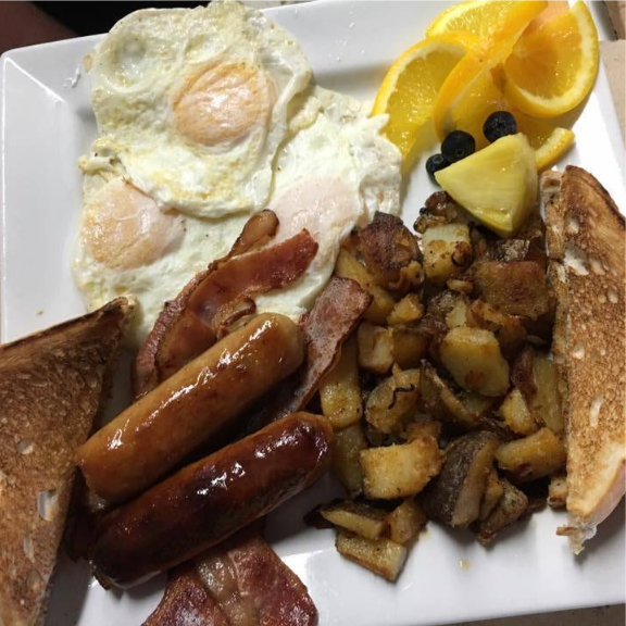 a white plate topped with eggs, sausage, toast and fruit.