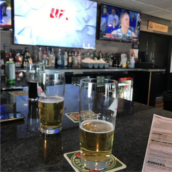 two glasses of beer sitting on a bar, with UFC on the TV