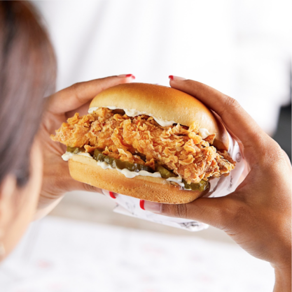 a woman holding a chicken sandwich in her hands.