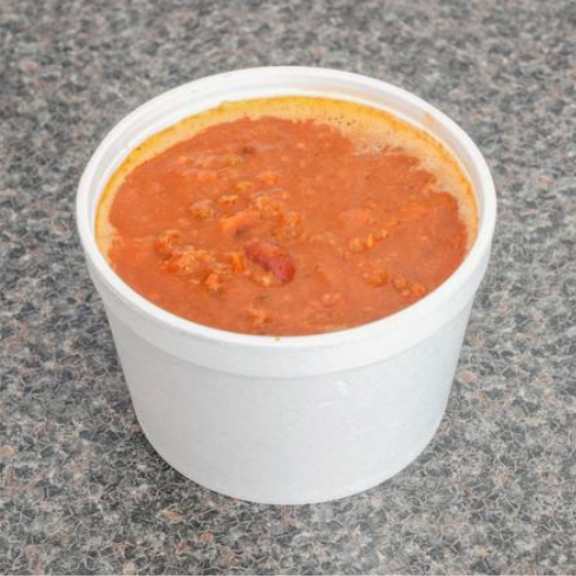 a white cup filled with red chili on top of a table.