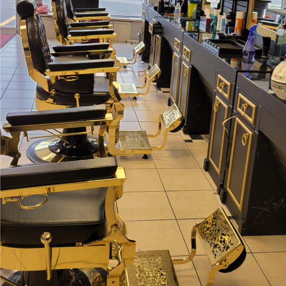 a row of black barber chairs with gold trim sitting on top of a tiled floor.