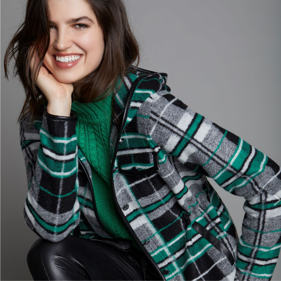 a smiling woman in a green sweater and black leather pants.