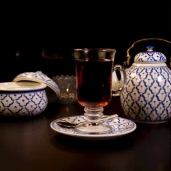 a glass of tea next to a teapot on a table.