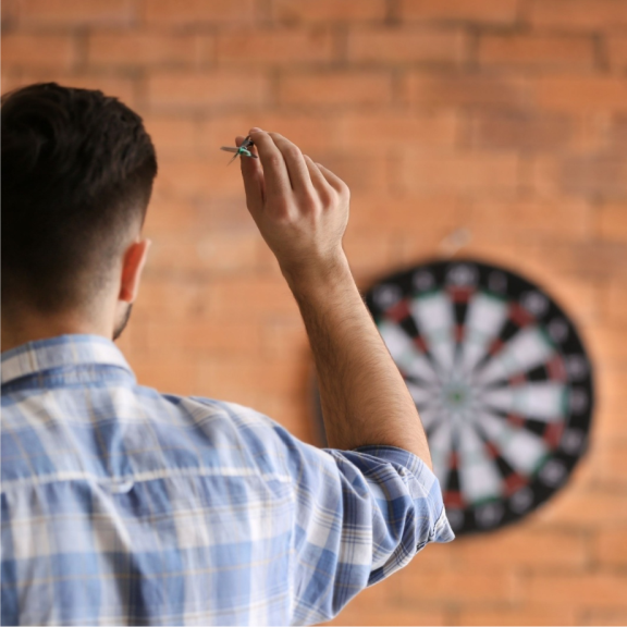 a man in a plaid shirt holding a dart in front of a brick wall.