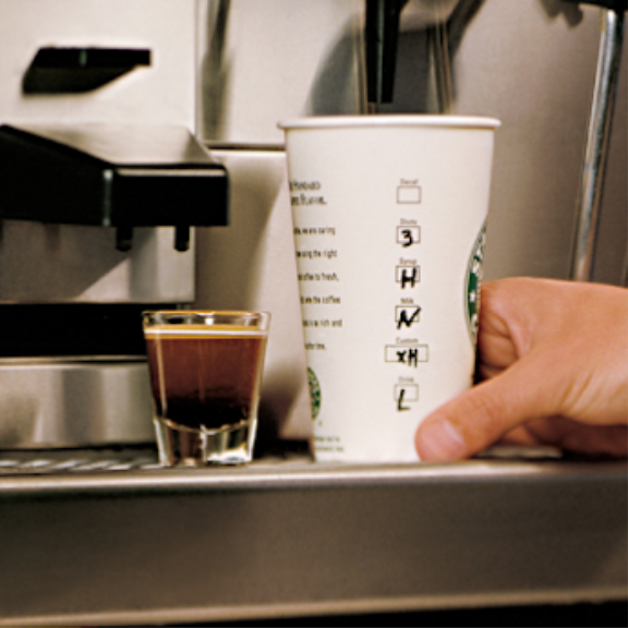 a person holding a coffee cup in front of a coffee machine.