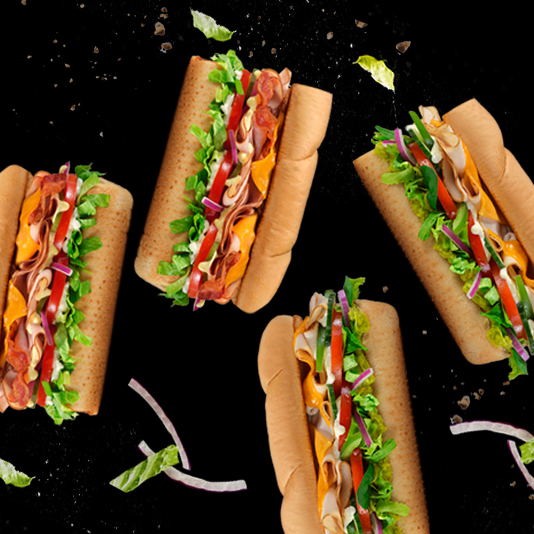 a group of four sub sandwiches sitting on top of a black surface.
