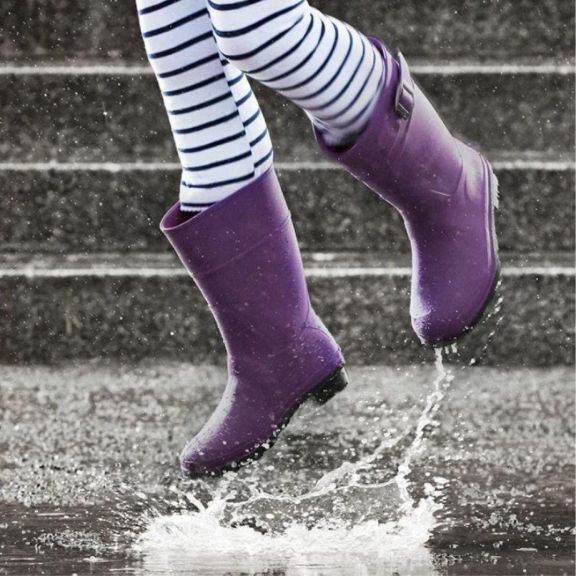 a kid in purple boots jumping into a puddle.
