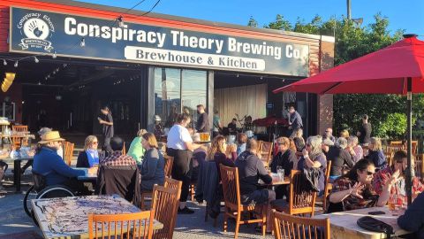 a group of people sitting outside of the conspiracy theory brewing cafe.