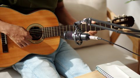 A man playing an acoustic guitar in front of a microphone.