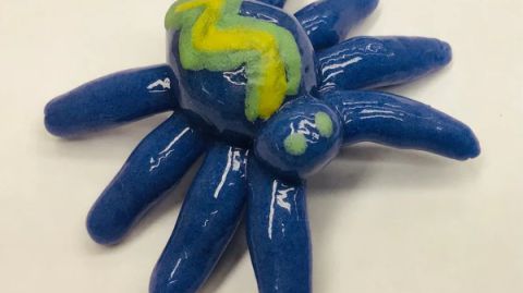 A blue and yellow ceramic spider on a white surface.
