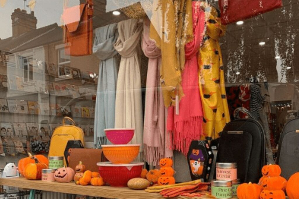 A window display with pumpkins, scarves, and bags.