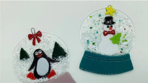 Two glass ornaments with penguins and snow globes.
