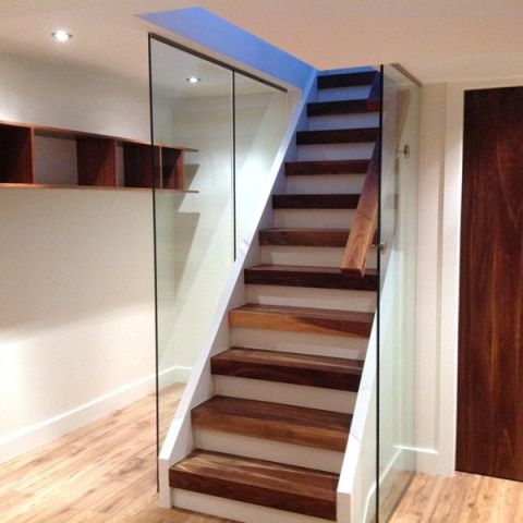 A wooden staircase with glass railings in a basement.