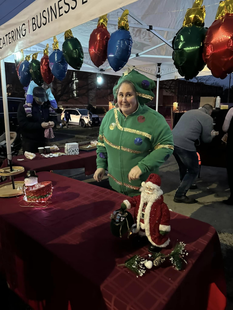 A woman in a santa costume standing in front of a table with balloons.