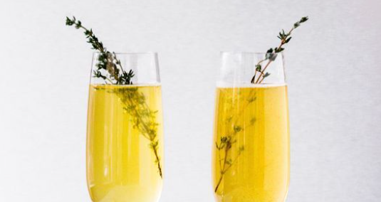 Two glasses of champagne with a sprig of thyme.