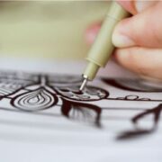 A person drawing with a pen on a piece of paper.