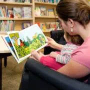 Young mom in the library, reading storybook with her daughter