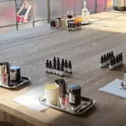 A large wooden table set up with trays containing candles, essential oil bottles, and other crafting supplies in a well-lit room.