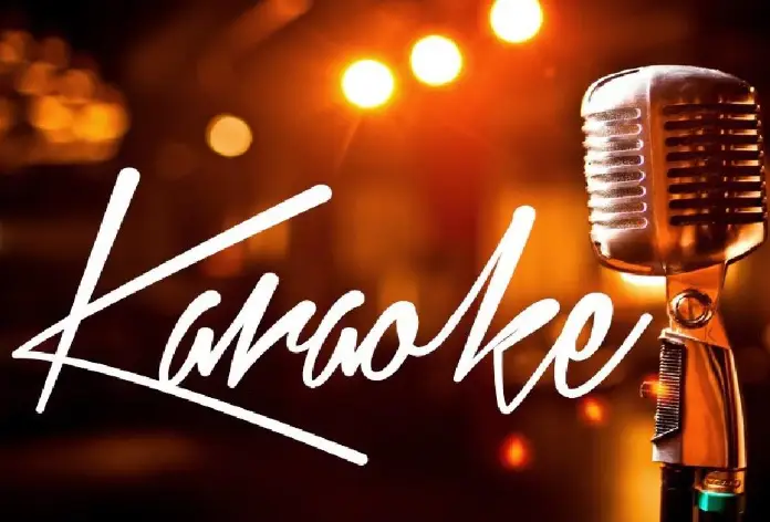 A vintage-style microphone with the word "Karaoke" in cursive script, set against a blurred background with warm, glowing lights.
