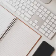 A neatly organized workspace with a keyboard, mouse, notebook, pen, glasses, smartphone, coffee cup, and a vintage camera.