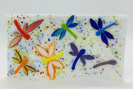 A wavy white panel with colorful dragonfly designs in various colors including red, orange, green, blue, and purple, set against a background with multicolored speckles.