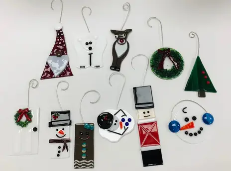 A collection of various glass Christmas ornaments, including festive characters like snowmen, a polar bear, a reindeer, a wreath, and geometrically shaped designs, with hooks for hanging.