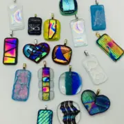 A collection of variously shaped and colorful fused glass pendants, including rectangles, hearts, and other shapes, displayed on a flat surface.