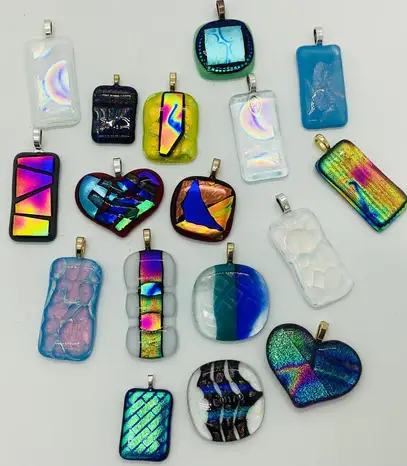 A collection of variously shaped and colorful fused glass pendants, including rectangles, hearts, and other shapes, displayed on a flat surface.